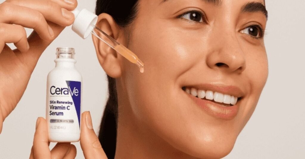 Smiling woman using a dropper to apply CeraVe Vitamin C Serum on her cheek.