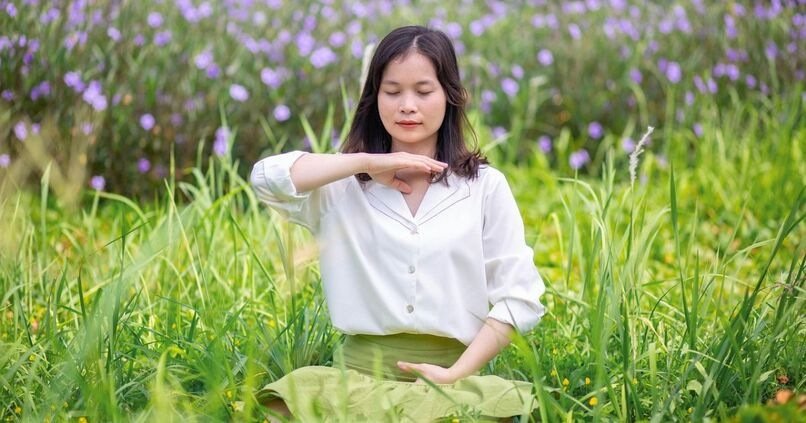 Woman practicing mindfulness meditation in a field of tall grass and purple flowers.